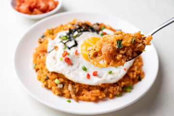 Kimchi fried rice with fried egg, pork, sesame seed, chili, spring onion and seaweed on white plate and eating, Korean food