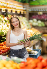 Blonde woman choosing green onions in supermarket. Customer stands in the grocery department and buys fresh herbs