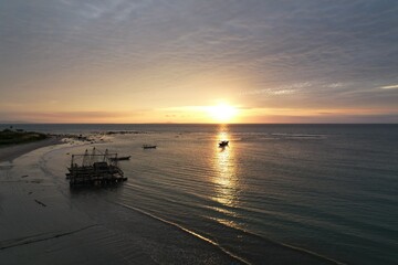 Beautiful sunset sky over the sea and background view of traditional fishermen's boats and floating cages. Seascape concept