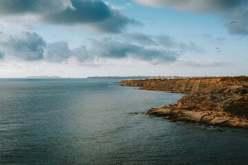 The rocky coastline stretches into the distance, meeting the vast expanse of the Atlantic Ocean under a dramatic, cloud filled sky, offering a breathtaking view of the Portuguese coast