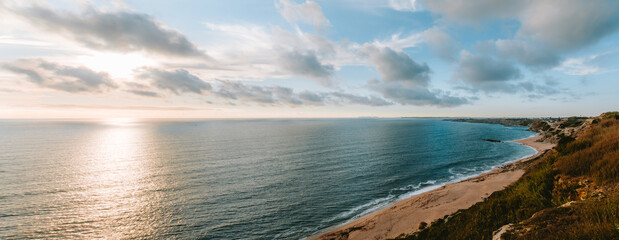 Golden sunset illuminating the calm waters of the Atlantic Ocean and the sandy beach of Peniche, Portugal, creating a serene and picturesque seascape