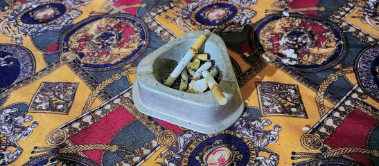 Old Ash Tray Full of Cigarette Butts on Ornate Fabric