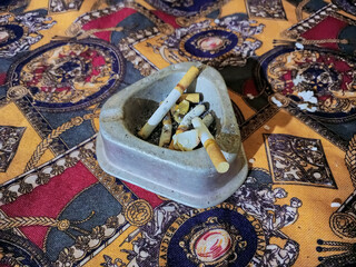 Old Ash Tray Full of Cigarette Butts on Ornate Fabric
