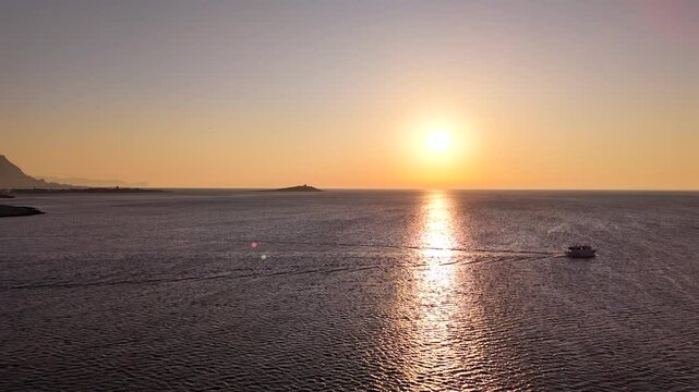 Peschereccio in navigazione nel golfo di sferracavallo accarezzato dal sole al tramonto durante una battuta di pesca estiva al gambero rosso di mazzara del vallo vista dall'alto con drone