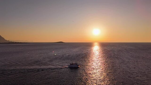 Peschereccio in navigazione nel golfo di sferracavallo accarezzato dal sole al tramonto durante una battuta di pesca estiva al gambero rosso di mazzara del vallo vista dall'alto con drone