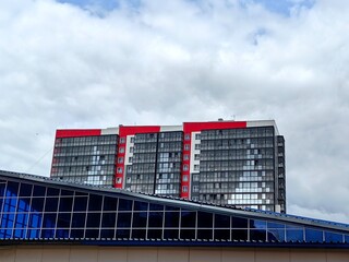 sleek, high rise building showcases mix red and glass facades, reflecting cloudy sky. surrounding...