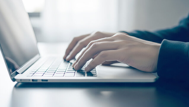 Hands typing on a laptop keyboard in a bright indoor setting.