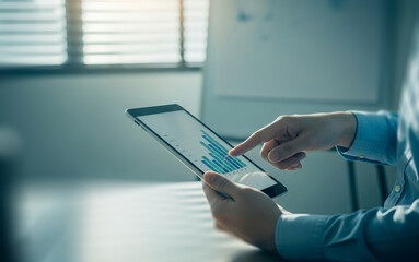 Obraz premium Hands using a tablet displaying a chart near a window with blinds.