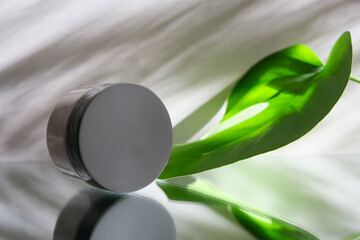 White jar with skincare product. Mirror reflection wet surface. Tropical nature. Wellness, mockup and beauty concept. Package