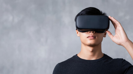 Young man using virtual reality headset against a gray background, exploring immersive digital experiences.