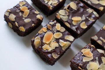 Chocolate Brownies cake pieces with topping almond slice on white background. Closeup and side view
