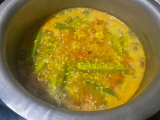 Khichdi being cooked in a pot in a home kitchen Drumstick vegetable, tomatoes, rice and spices