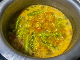 Khichdi being cooked in a pot in a home kitchen Drumstick vegetable, tomatoes, rice and spices