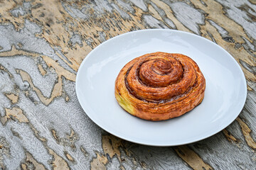 close up view of one sweet Cinnamon roll dessert on white plate. Isolated on wooden table background. copy space, empty, free, negative.