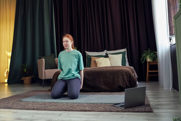 Woman practices yoga in a cozy room with a laptop during a quiet afternoon session