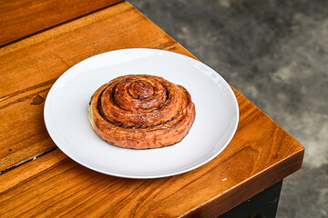 Close up view of one sweet Cinnamon roll dessert on white plate. wooden table background. corner. grey or gray cement floor.