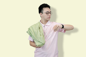Young Asian man in a casual polo shirt and glasses, holding a jacket over his shoulder, checking...