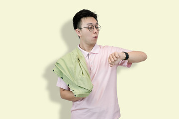 Young Asian man wearing glasses and a polo shirt, holding a jacket, looking at his wristwatch with...