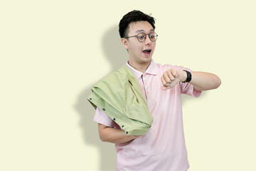 Young Asian man wearing glasses and a polo shirt, holding a jacket, looking at his wristwatch with...
