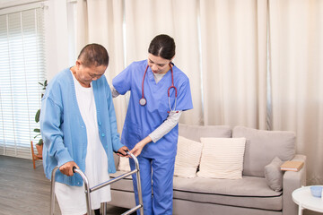 Young nurse assisting senior woman in walking with a walker, demonstrating caregiving,...