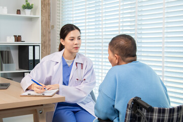 Female doctor consulting senior patient across table, pointing at laptop screen while discussing...