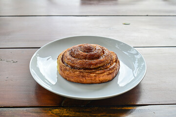 close up view of one sweet Cinnamon roll dessert on white plate. Isolated on wooden table background. copy space, empty, free, negative.
