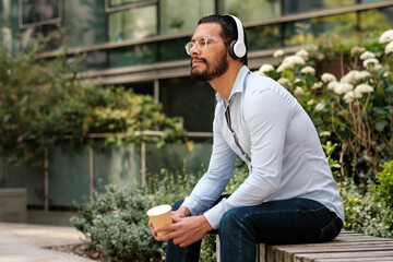 Businessman listening music with headphones and holding coffee outside office