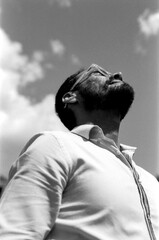 Man wearing glasses looking up at cloudy sky in monochrome analog photo