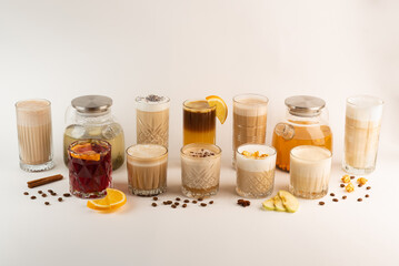 A variety of autumn drinks in glasses, including coffee, tea, and mulled wine, arranged in a row on a white background