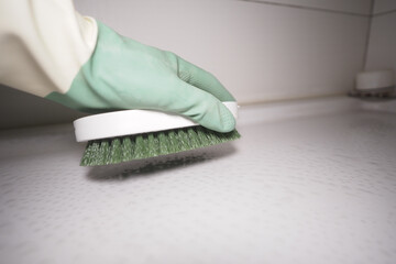 Hand Cleaning a Surface Using a Green Brush and Protective Gloves
