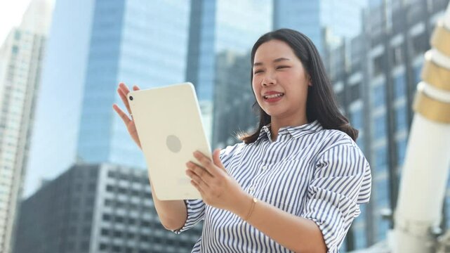 slow motion scene young beautiful asian businesswoman hold digital tablet device while looking forward to building tower at city town outside for business achievement and vision forward concept