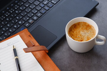 淹れたての美味しいコーヒーを飲みながら、ノートパソコンとシステム手帳でデスクワークをしているイメージ
