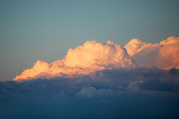 Giant orange cumulus puffy clouds coloured by a setting sun against a blue sky backdrop.
