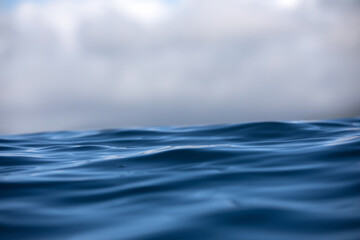 Close-up sea level view of blue rippling ocean's surface under a stormy cloud-filled sky.