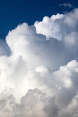Beautiful textured layered white clouds in a deep blue sky captured from below in portrait orientation.