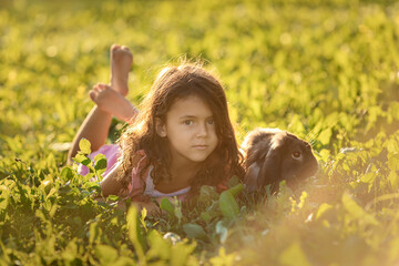Summer portrait of child toddler girl lying on the grass with brown rabbit