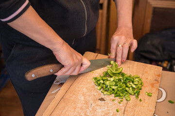 a person dicing green bell peppers on a wooden cutting board using a chef's knife. This is a common food preparation technique used in cooking for various dishes, such as stir-fries, salads, or sauces
