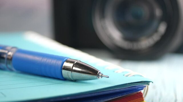 Close-up of pen and notebook with camera in background