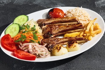 Lamb rack with vegetables, rice, and fries in bright lighting, overhead composition