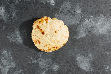 Tandoor flatbread on moody stone surface, overhead minimal composition with rustic texture