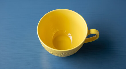 Yellow Ceramic Cup Centered On Blue Surface Showing Interior Details and Handle in a Minimalist Studio Setting