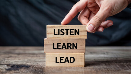 Hand stacking wooden blocks with the words listen learn lead symbolizing personal growth and leadership development journey