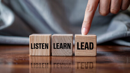 Finger pointing to wooden blocks with the words listen learn lead symbolizing personal development and career progression
