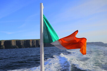 Irish Flag Waving on Boat Tour near Cliffs of Moher, County Clare, Ireland – Scenic Ocean View with Dramatic Coastal Cliffs and Blue Sky on a Bright Sunny Day along the Wild Atlantic Way