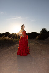 A breathtaking and stunning model elegantly poses in a flowing red dress against a beautiful sunset backdrop