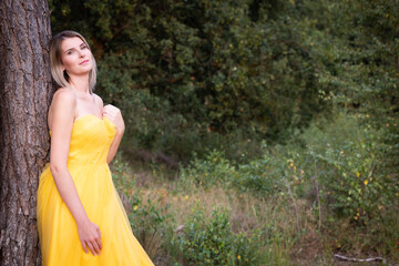 In a serene moment, a woman gracefully poses in a flowing yellow dress amidst a stunningly lush green backdrop