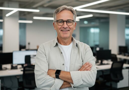 Smiling mature businessman with glasses and crossed arms in a modern office setting