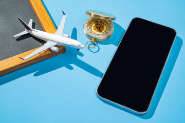 Small chalkboard, airplane, compass, and cellphone on blue background. Mockup or Copy space. Travel...