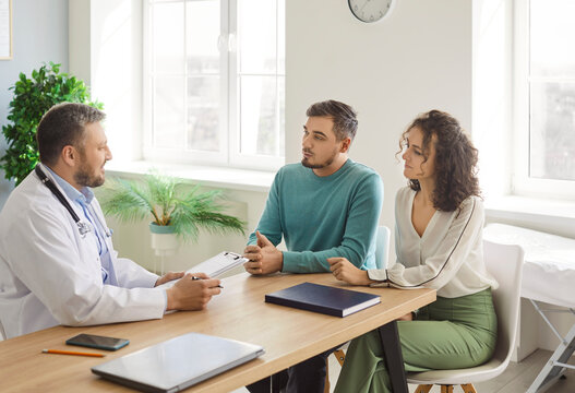 Doctor talking, meeting, consulting happy couple patients in fertility clinic, offering help, giving medical advice, professional clinician talking to husband, wife planning pregnancy, test check exam