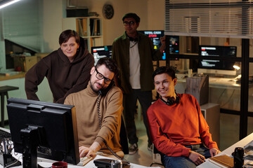 Group of people of diverse ethnicities operating computers and headsets in office at night,...